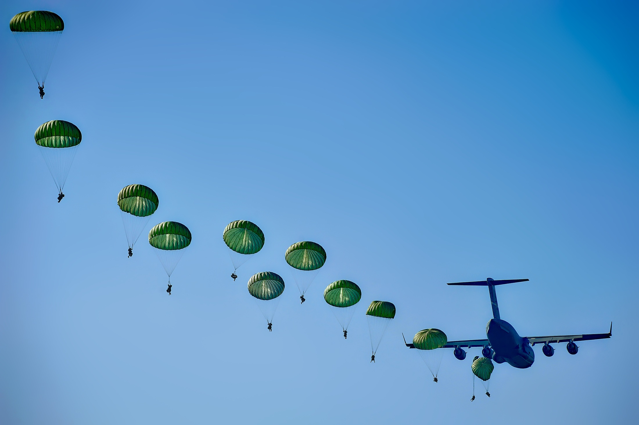 Parachutistes militaires en formation descendant du ciel bleu derrière un avion de transport.