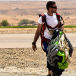 Un instructeur de sauts en parachute marche sur un terrain plat, portant son parachute partiellement replié.