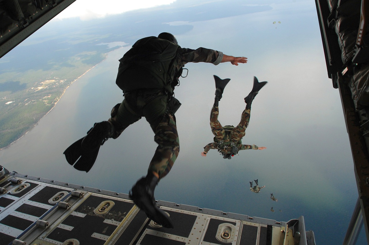 Deux militaires en tenue de camouflage sautant d'un avion, au-dessus de la côte avec la mer en fond