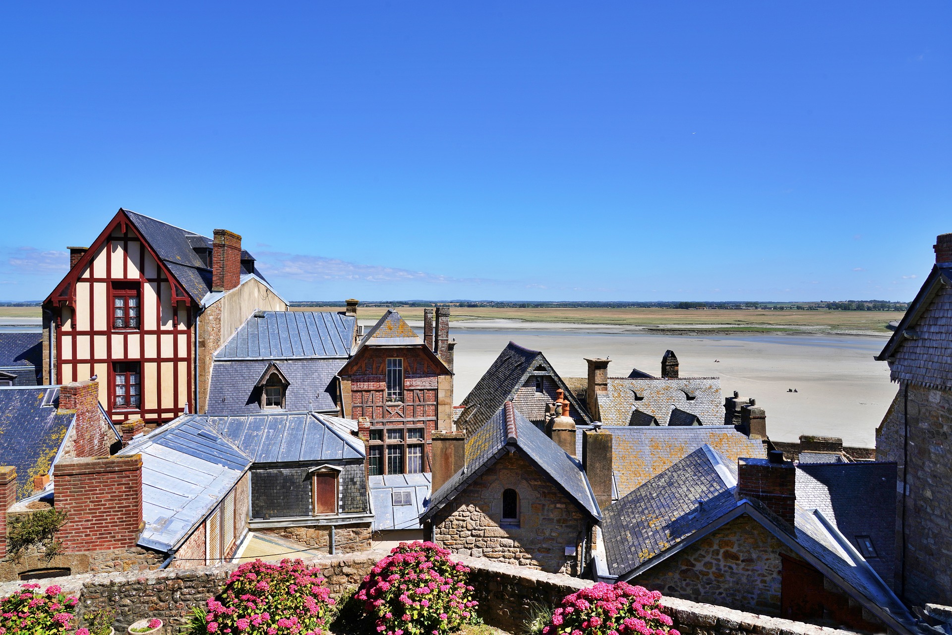 Vue d'habitations bretonnes en premier plan et en arrière plan la mer et un ciel d'un bleu vif.