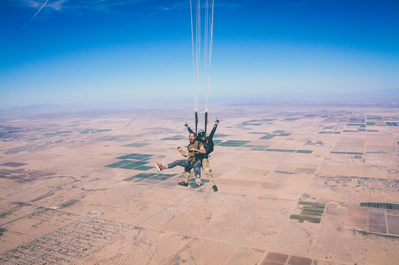Un parachutiste souriant en chute libre, les bras ouverts, au-dessus d'un paysage désertique quadrillé de parcelles de terres agricoles